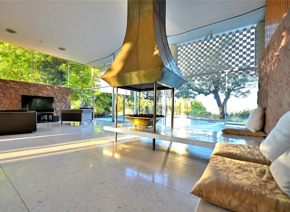 Filberg House living room with stone fireplace, copper hood and glass walls.